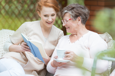 caregiver reading the book while senior woman is listening at the garden